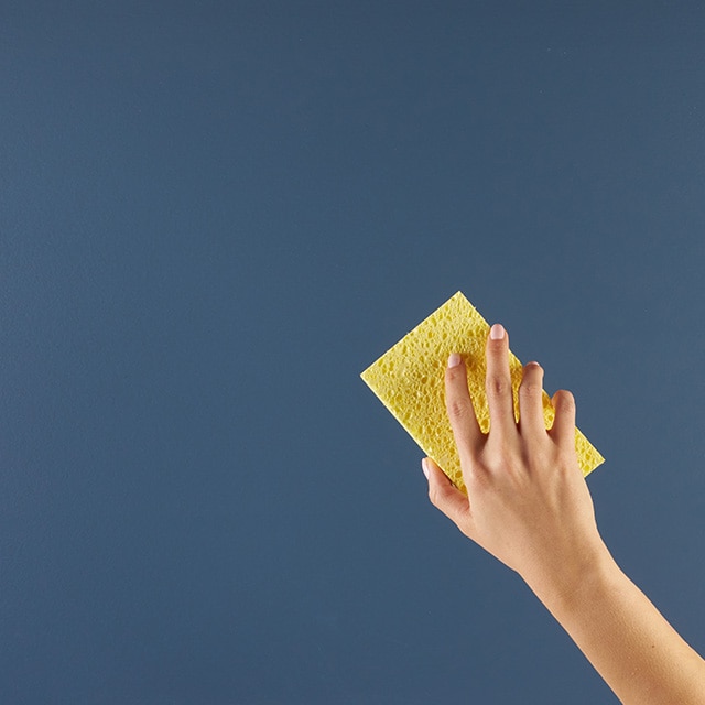 A blue painted surface being cleaned gently with a sponge